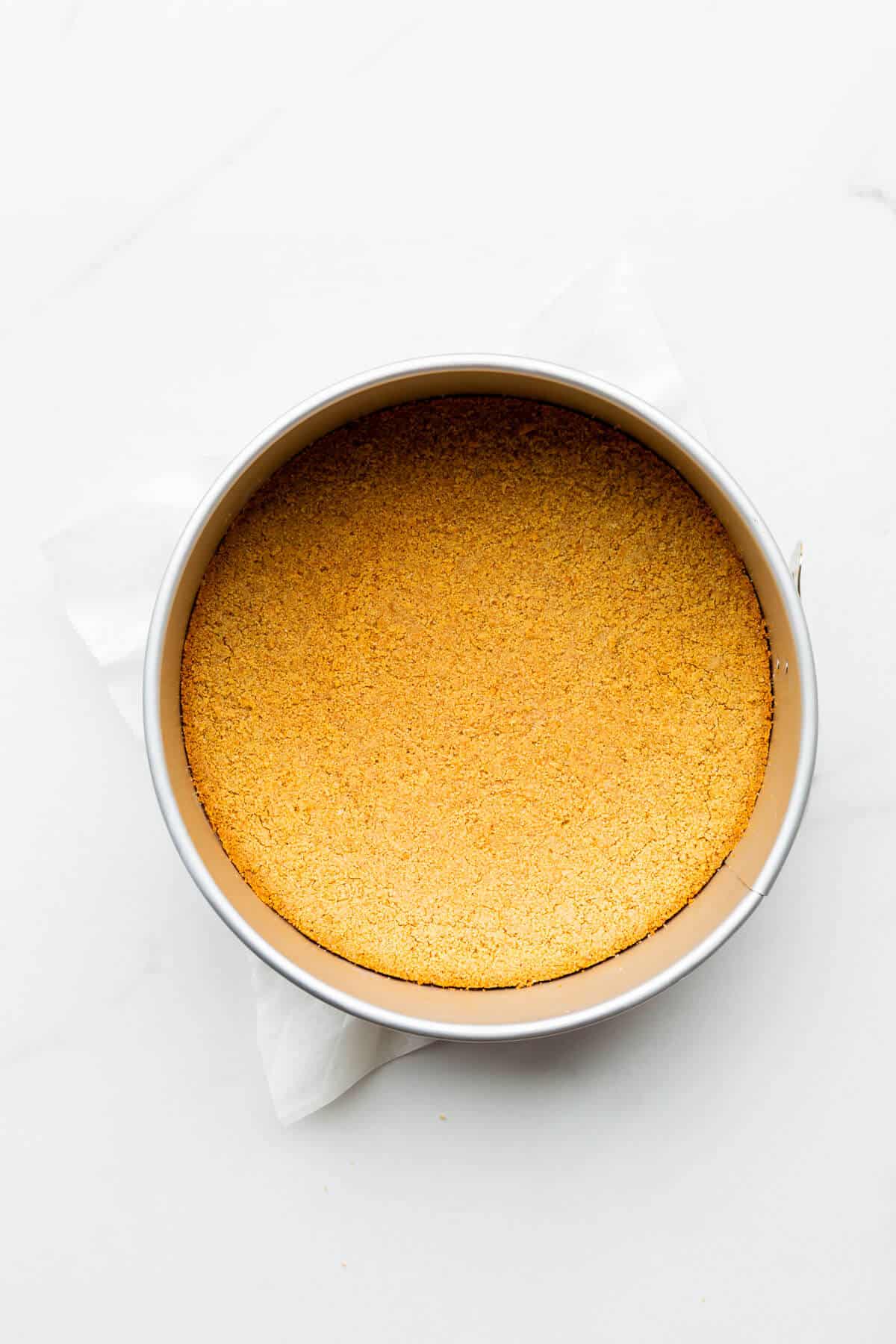 A baked graham cracker crust in a springform pan, perfectly smooth with a slightly golden edge that is beginning to separate from the walls of the pan.