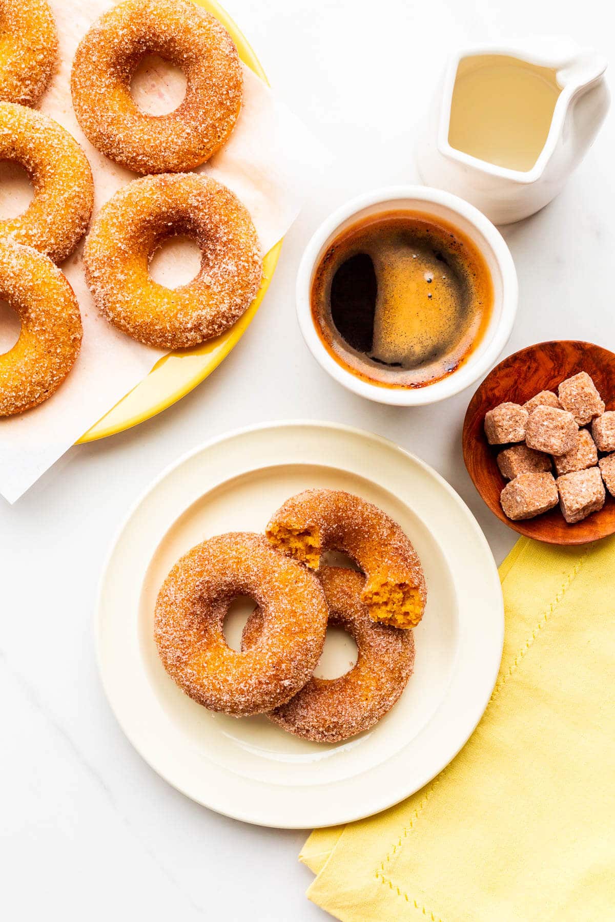Plates of baked pumpkin donuts coated in cinnamon sugar and served with coffee.