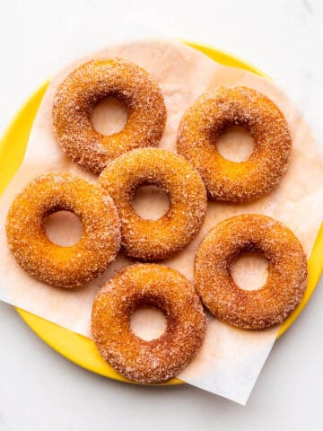 A yellow plate of baked pumpkin donuts coated in cinnamon sugar.