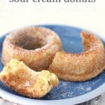 Baked sour cream donuts, one broken in half, coated with granulated sugar on a blue plate with floral napkin underneath