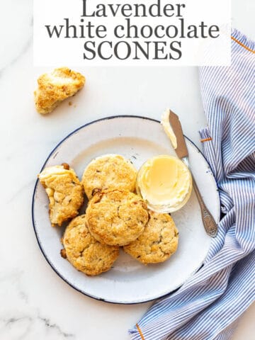 Baked lavender white chocolate scones on a blue-rimmed white enamelware plate with butter and a butter knife, blue and white striped napkin