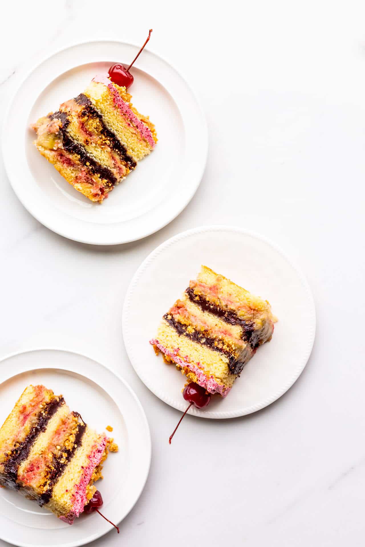 Slices of banana split cake topped with maraschino cherries, served on plates.
