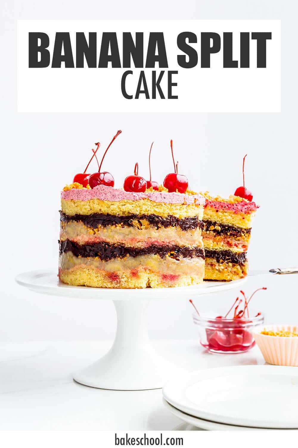 Banana split layer cake topped with maraschino cherries on a cake stand.