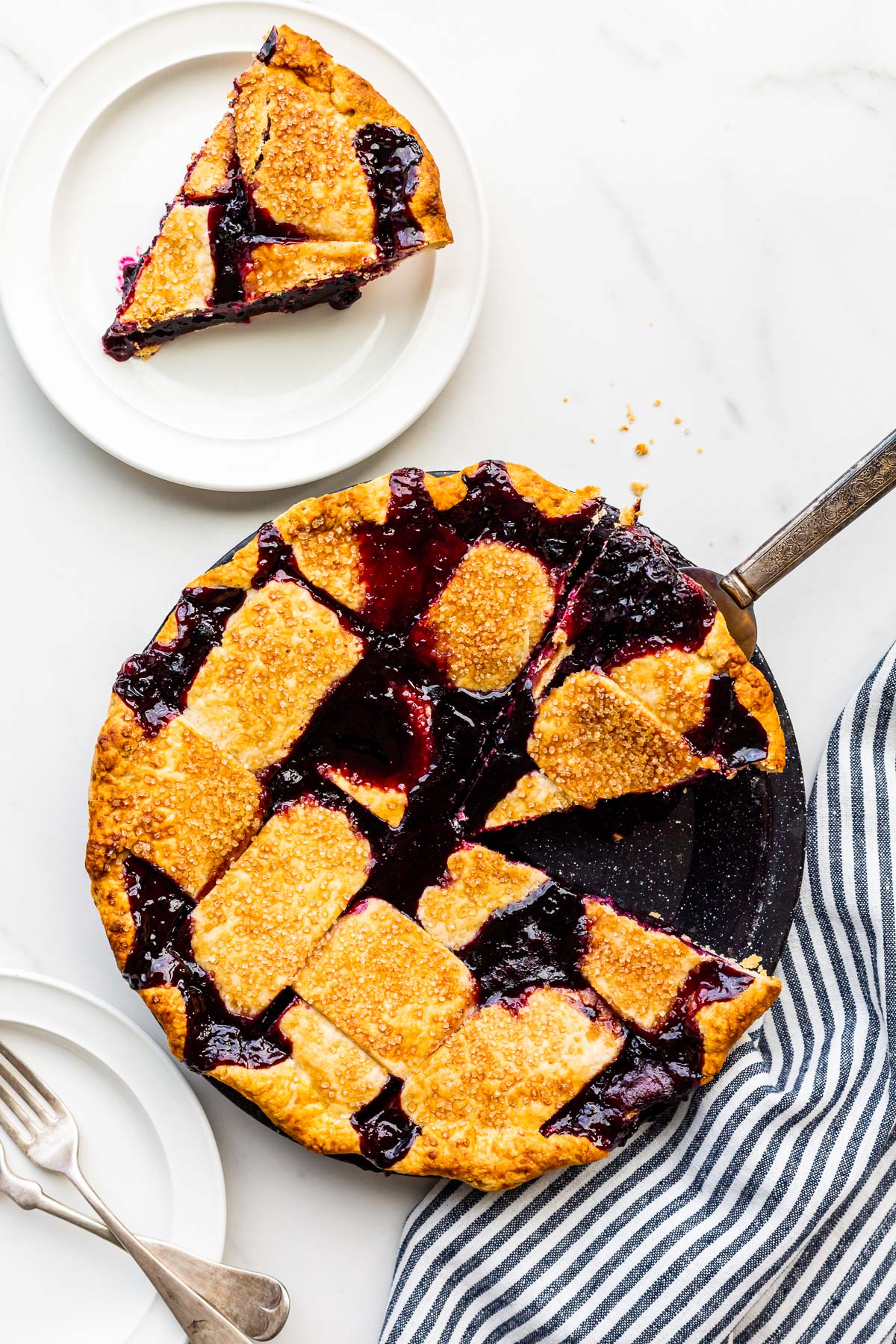 Freshly baked blueberry pie being sliced and served on plates.
