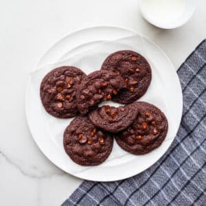 A plate of chocolate chocolate chip cookies with a glass of milk.