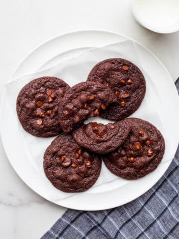 A plate of chocolate chocolate chip cookies with a glass of milk.