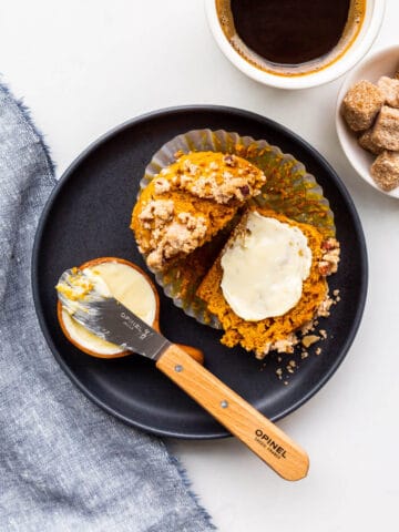 A plate with a pumpkin muffin split open and smeared with butter, with a cup of coffee on the side.