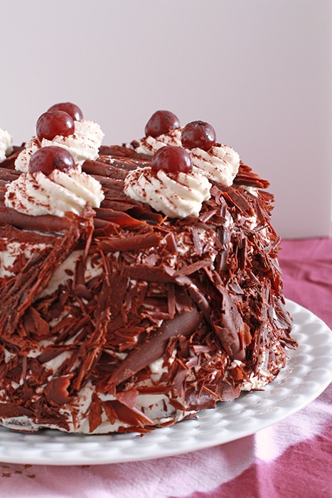 gâteau forêt noire coated in whipped cream and shaved dark chocolate, served on a white plate,