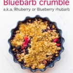 Blueberry rhubarb crumble with a marzipan oat crumble topping served in a round ceramic blue baking dish with a fluted edge
