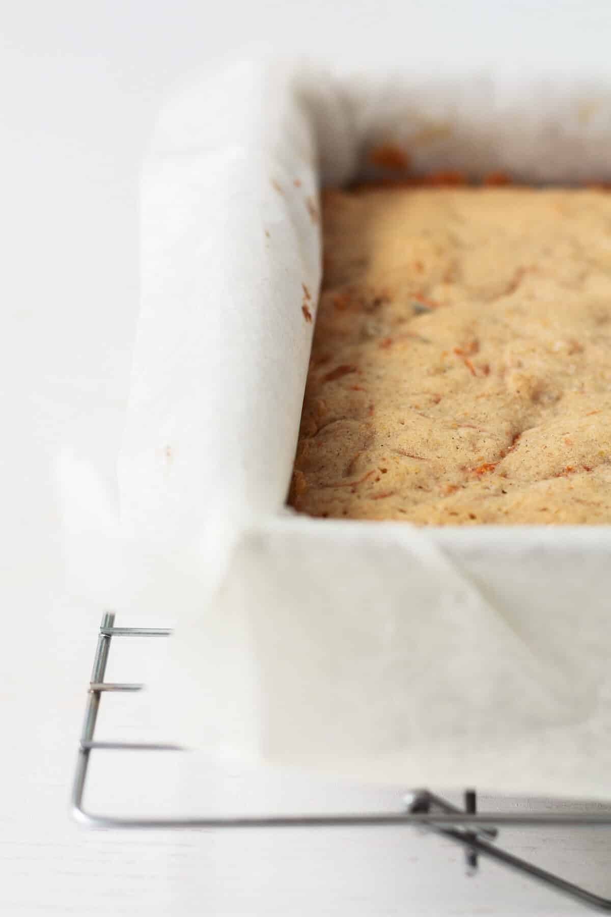 A parchment paper-lined square pan of carrot cake after baking.
