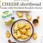 Savoury cheese shortbread cut into oak leaf shapes on a speckled plate with a box of Rondelé cheese, salt and pepper.