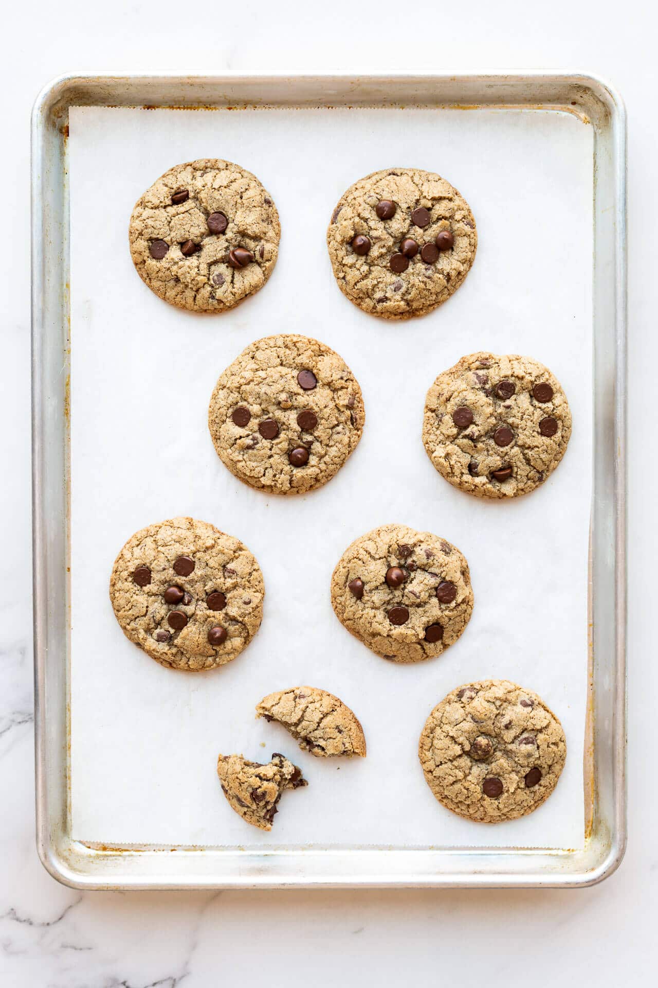 Thick chewy chocolate chip cookies made with buckwheat flour so they are a little greyer in colour compared to all-purpose flour and baked on a parchment lined sheet pan (8 cookies, one of which is broken in pieces)