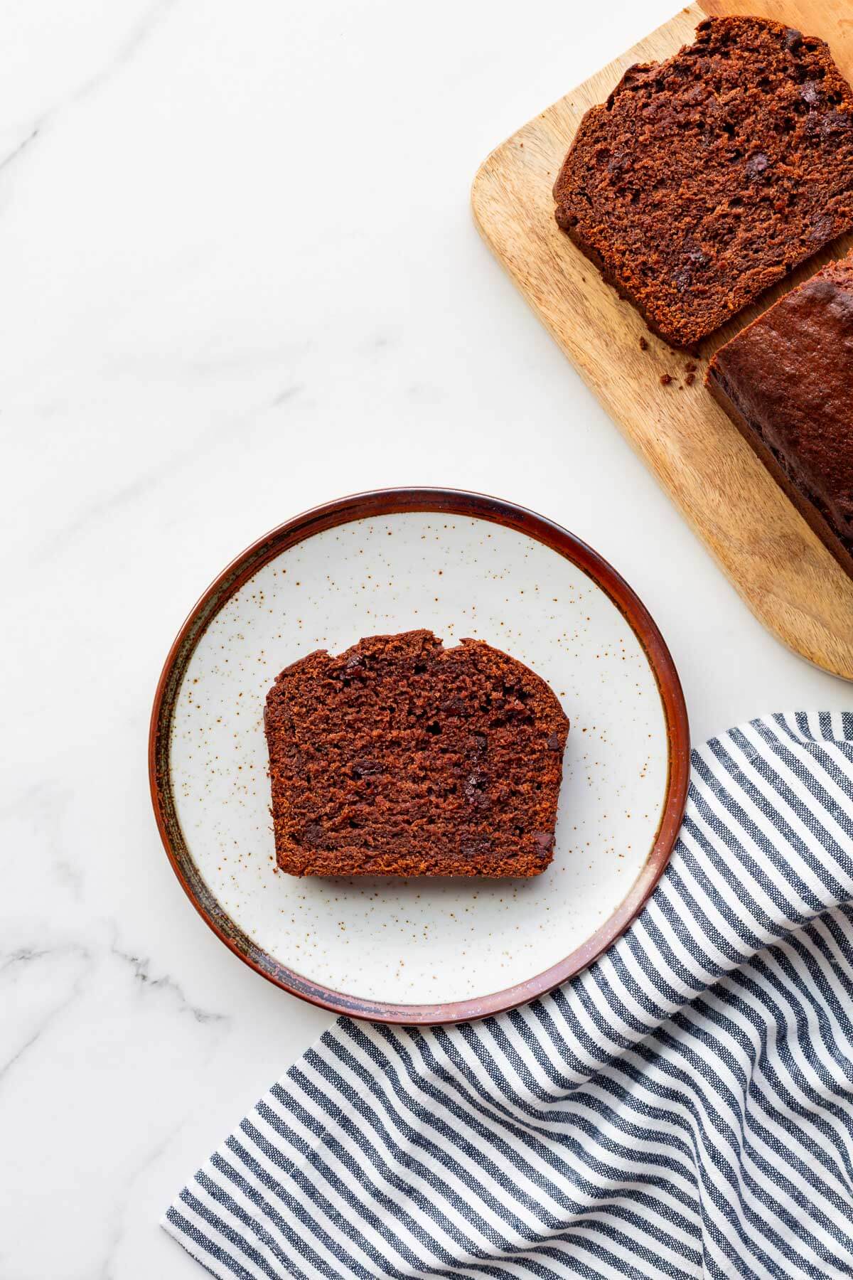 A slice of chocolate banana bread on a plate with a striped napkin on the side.