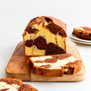 Slicing a chocolate and vanilla marble cake on a cutting board.