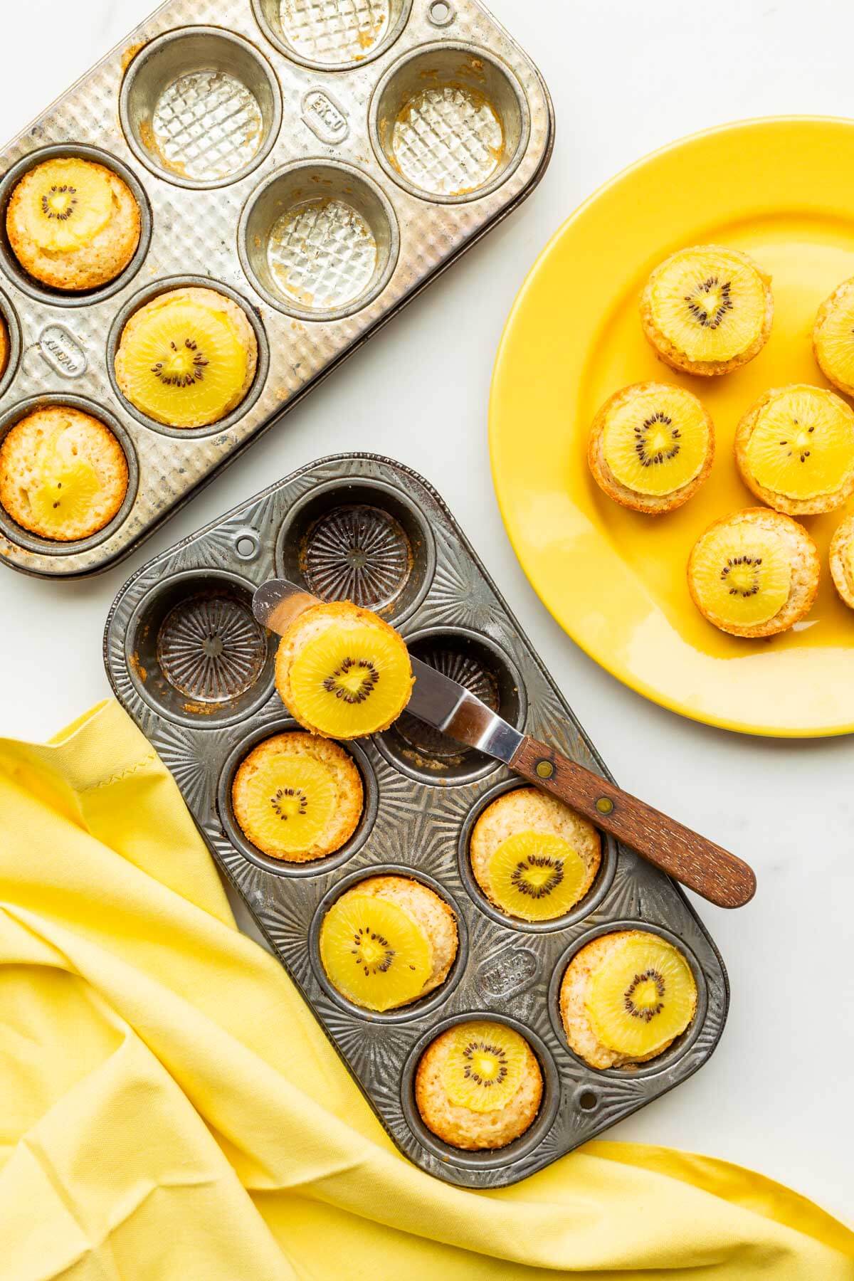 Unmoulding little golden kiwi cakes from a mini muffin pan with the help of a mini offset spatula to serve them.