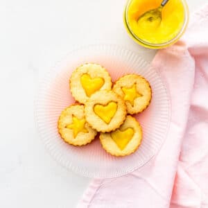 A plate of lemon curd-filled shortbread cookies with a jar of lemon curd on the side.
