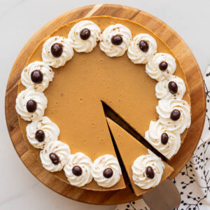 Serving a slice of a coffee-flavoured cheesecake with whipped cream piped around the border and chocolate-covered coffee beans.