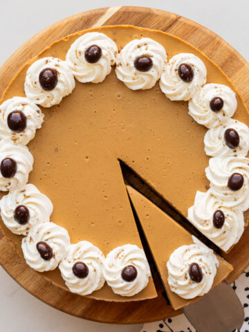 Serving a slice of a coffee-flavoured cheesecake with whipped cream piped around the border and chocolate-covered coffee beans.