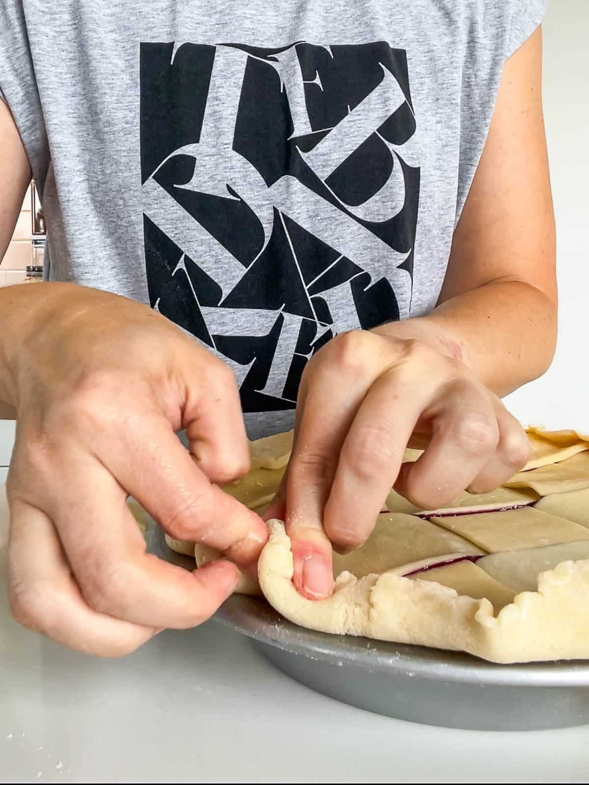 Crimping the edge of a double crust pie with fingertips to seal the two layers of dough together and create a decorative edge.