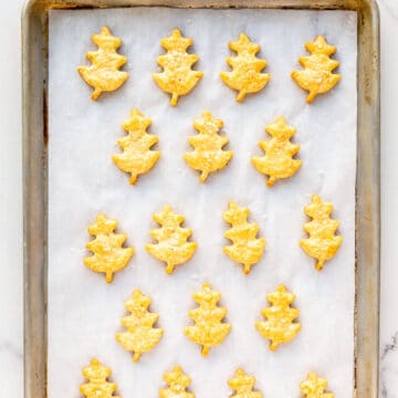 Freshly baked cheese shortbread cookies shaped like oak leaves on a parchment-lined baking sheet