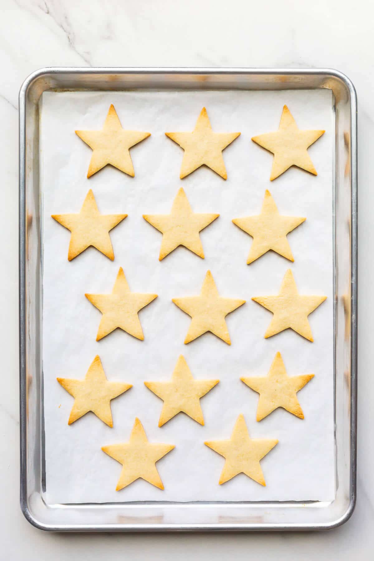 Star sugar cookies on a parchment-lined sheet pan after baking.