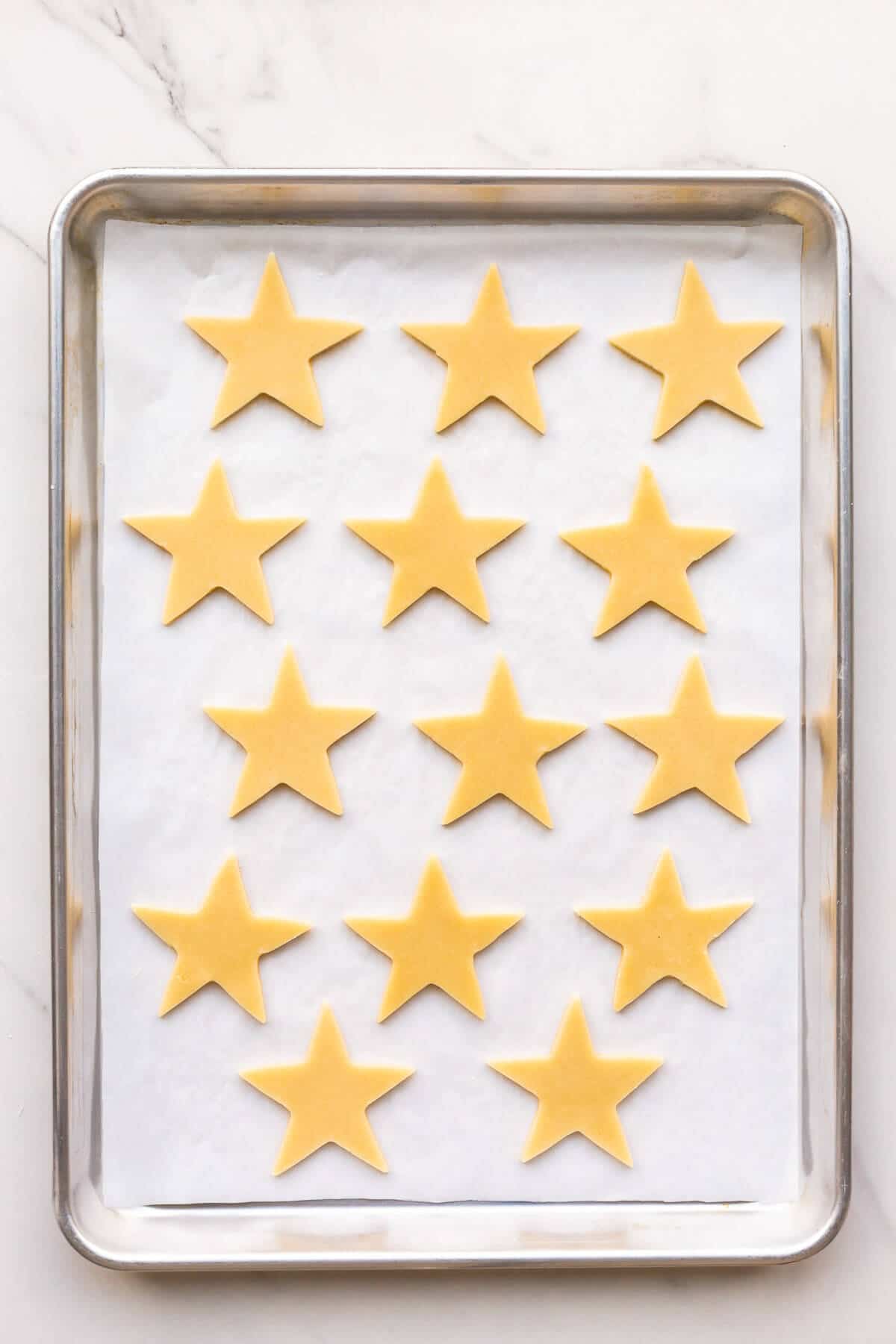 Star sugar cookies on a parchment-lined sheet pan before baking.