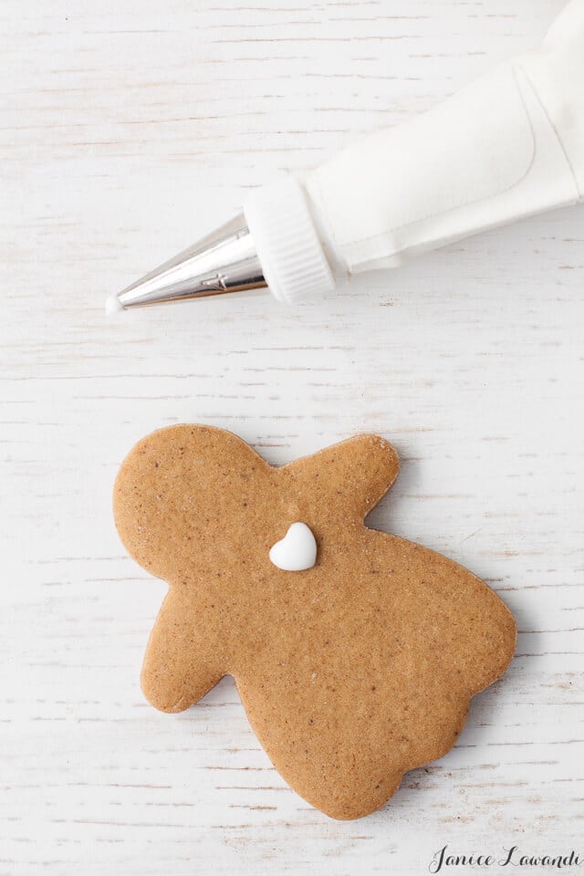 A gingerbread girl being decorated with royal icing with a heart piped on her chest.
