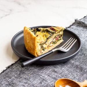A slice of quiche with rainbow Swiss chard in it, served with a small bowl of salt on the side.