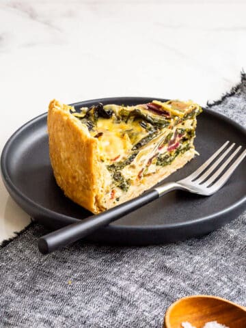 A slice of quiche with rainbow Swiss chard in it, served with a small bowl of salt on the side.