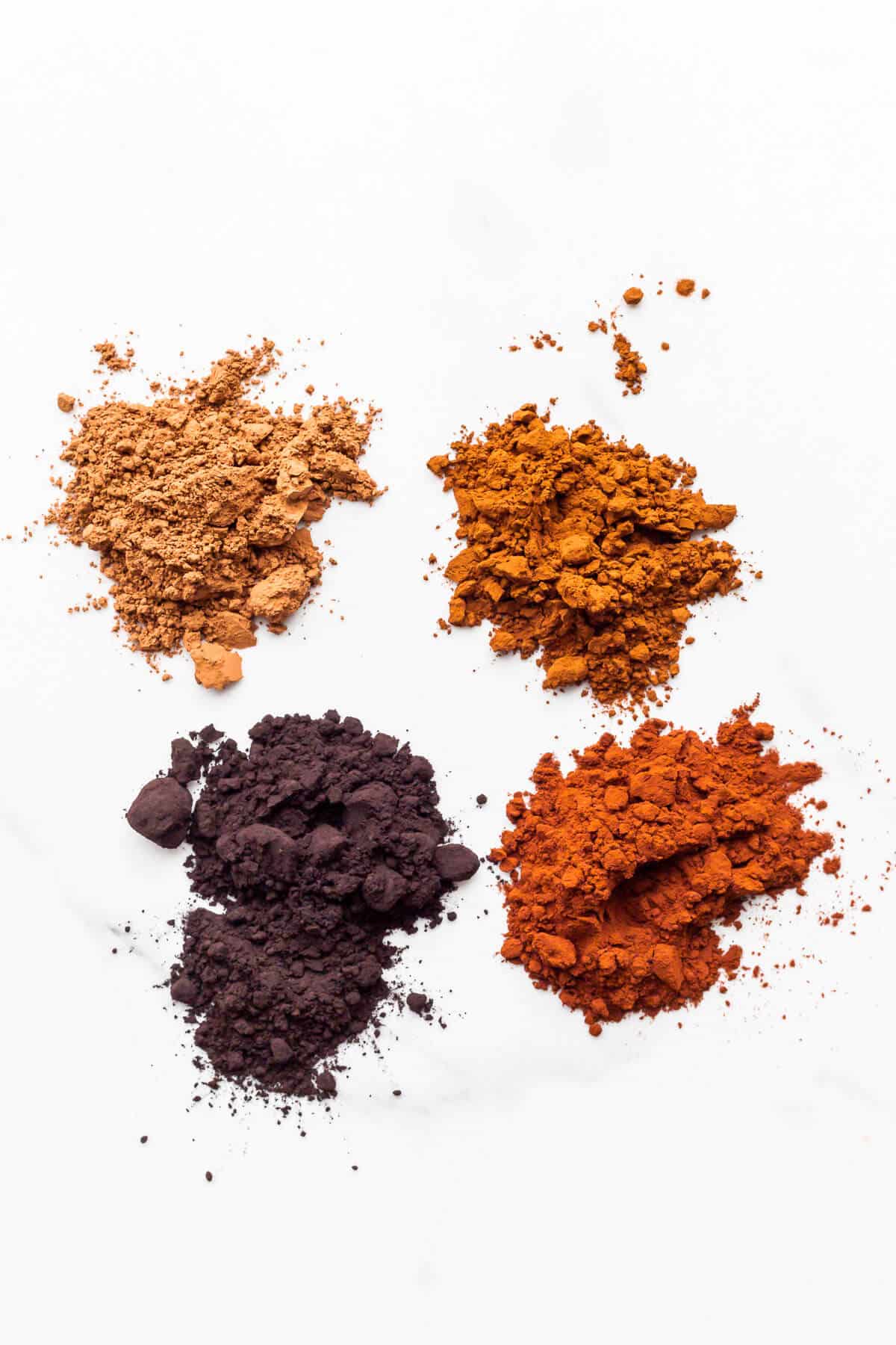 Small mounds of different types of cocoa powders, which range in colour from light brown to black.
