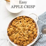 Easy apple crisp baked in a speckled white round baking dish set next to blue and white striped linen with a serving spoon, white bowls and wooden spoons