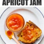 A jar of apricot jam served with toast on a plate.