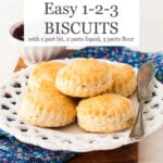A pile of plain biscuits on a white plate with a knife, blue floral napkin (Liberty style floral pattern)