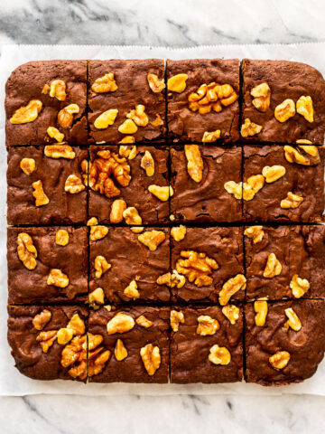 Brownies with walnuts cut into squares on a marble surface.