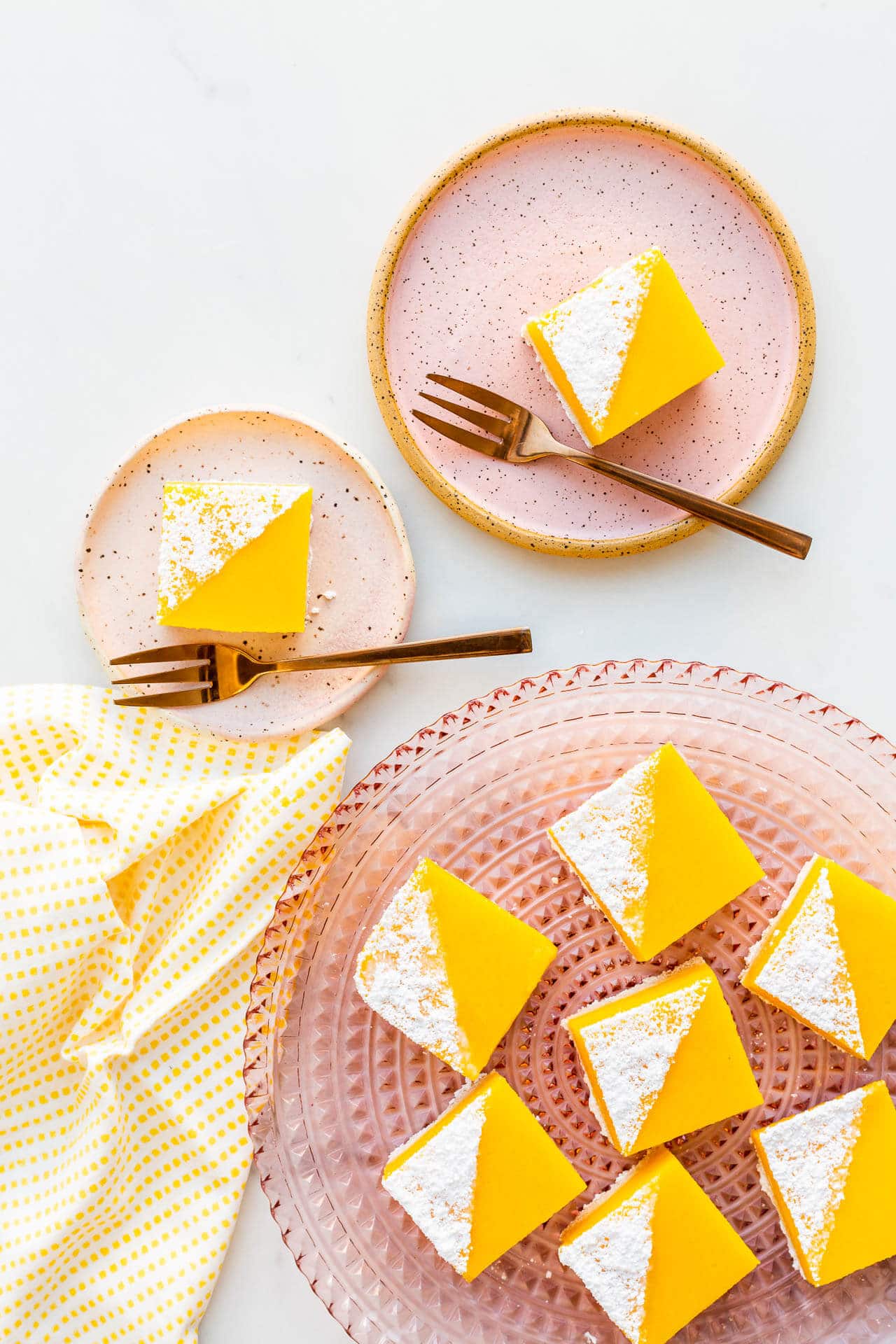 A pink glass plate with lemon bars topped with powdered sugar, ready to serve.