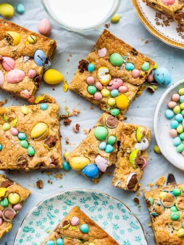 Mini Egg bars cut into squares and served on small plates with a glass of milk on the side and a bowl of Mini Eggs.