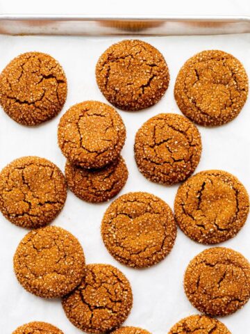 Freshly baked molasses cookies coated in turbinado sugar on a parchment-lined sheet pan.
