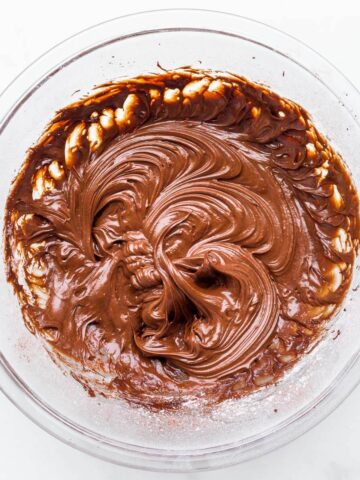A glass bowl of glossy chocolate sour cream frosting.
