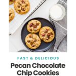 Serving pecan chocolate chip cookies from a cooling rack onto a black plate with a glass of milk.