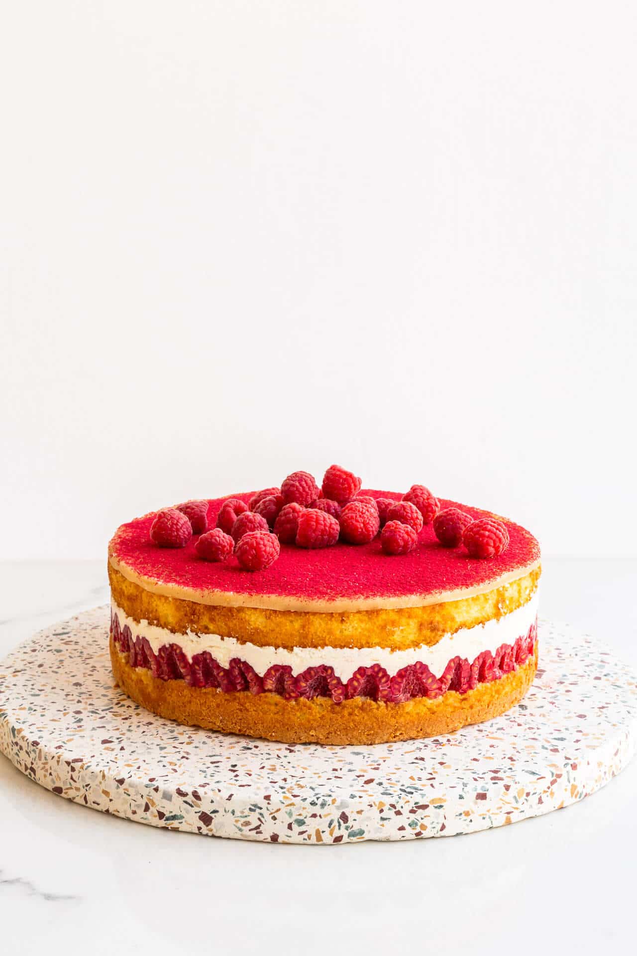Raspberry layer cake on a terrazzo stone board.