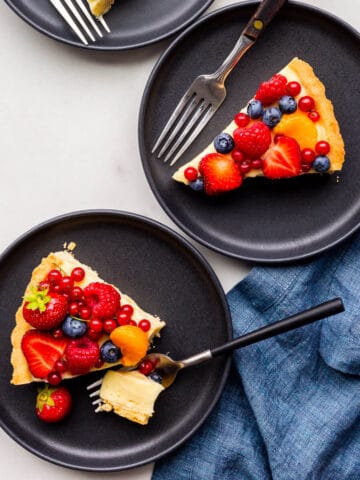 Slices of fruit tart served on black dessert plates.