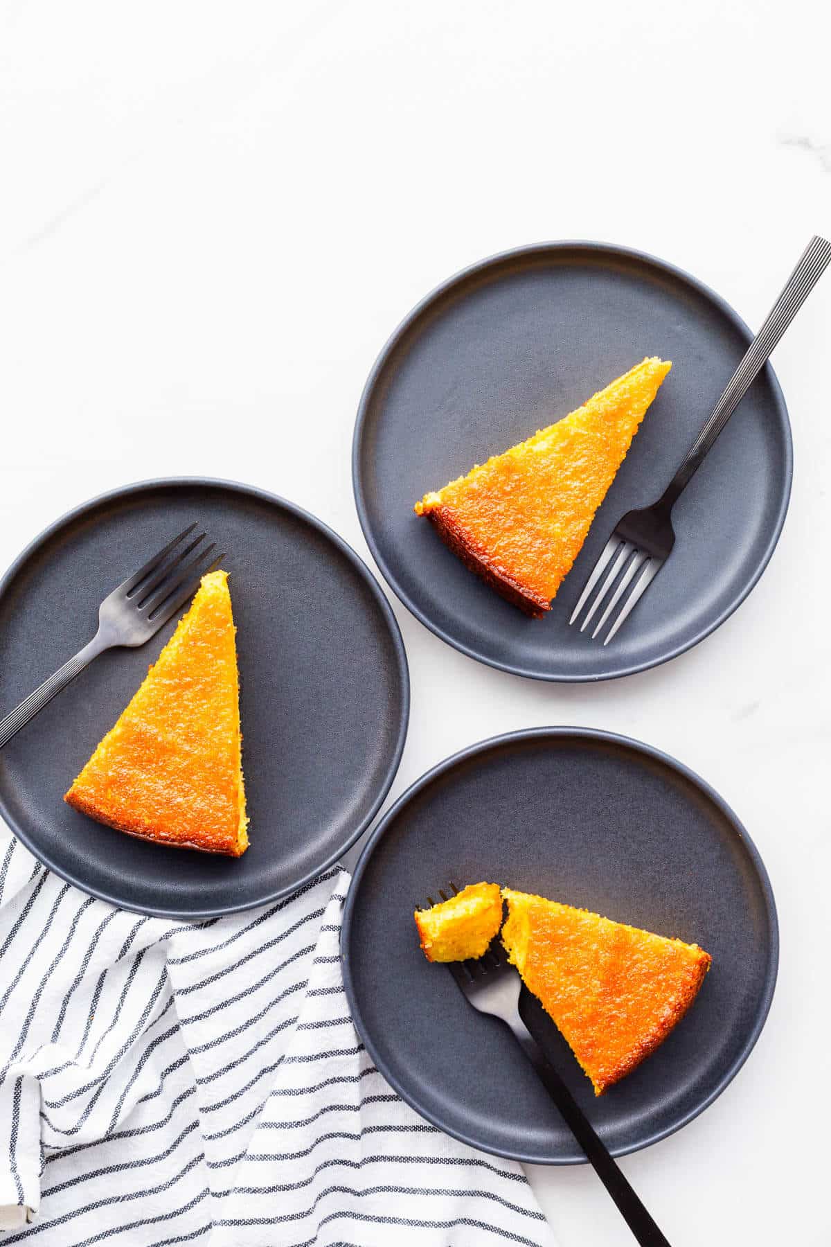 Slices of orange cake on black plates with black forks.