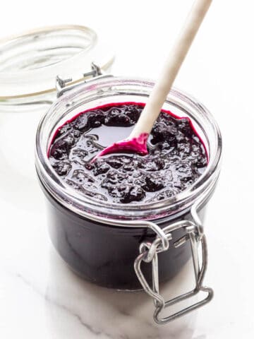A jar of homemade blueberry jam with a spoon.