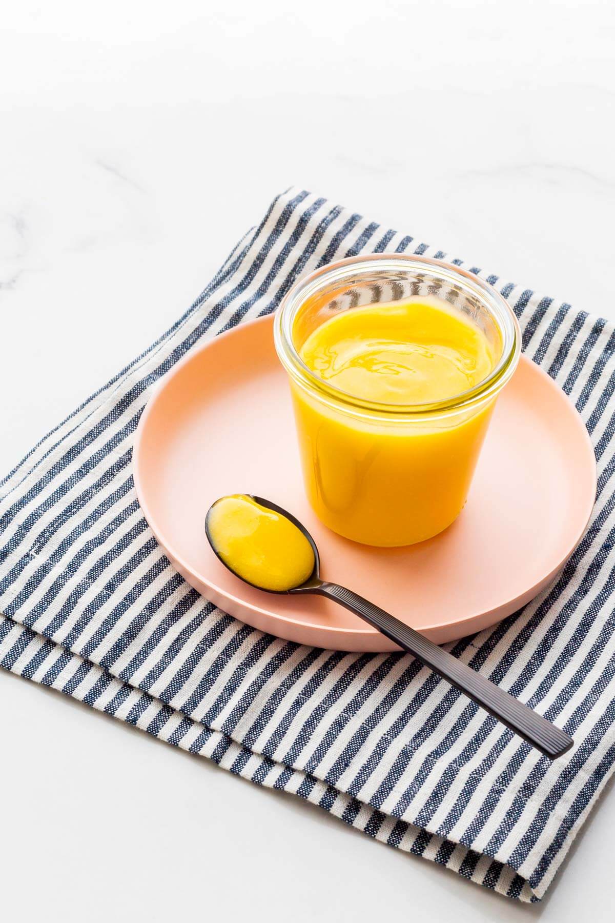 A jar of lemon curd on a pink plate with a napkin.