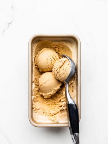Scooping homemade black tea infused ice cream frozen in a loaf pan with a black handled ice cream scoop