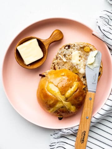 Hot cross bun on a pink plate split open and served with butter.
