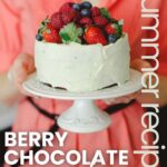 A layer cake topped with fresh berries on a cake stand.