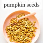 A pink bowl of toasted pumpkin seeds with a pink spoon for serving them