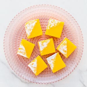 A pink glass plate with lemon bars.