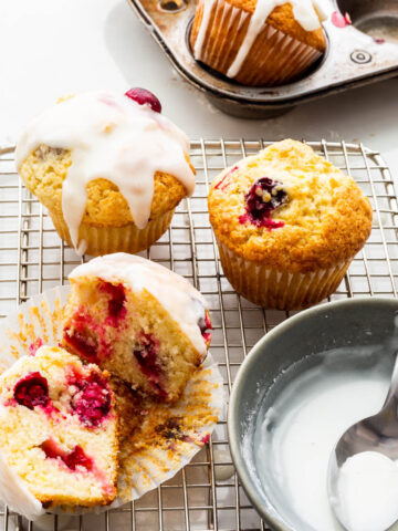 Drizzling lemon cranberry muffins on a wire rack with lemon icing.